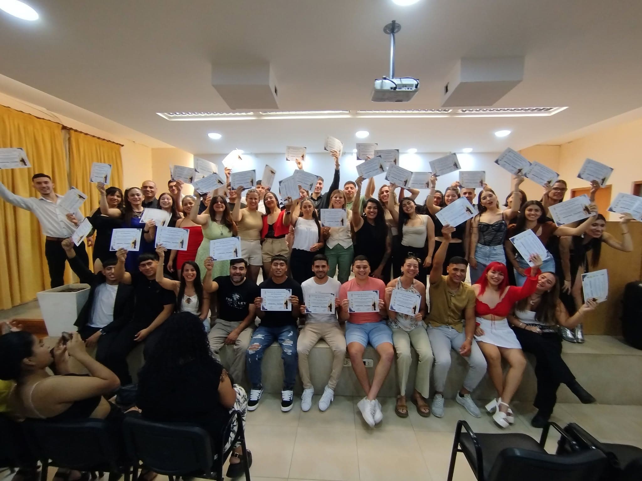 Grupo de estudiantes sonrientes posando con sus certificados en alto durante una ceremonia de graduación.
