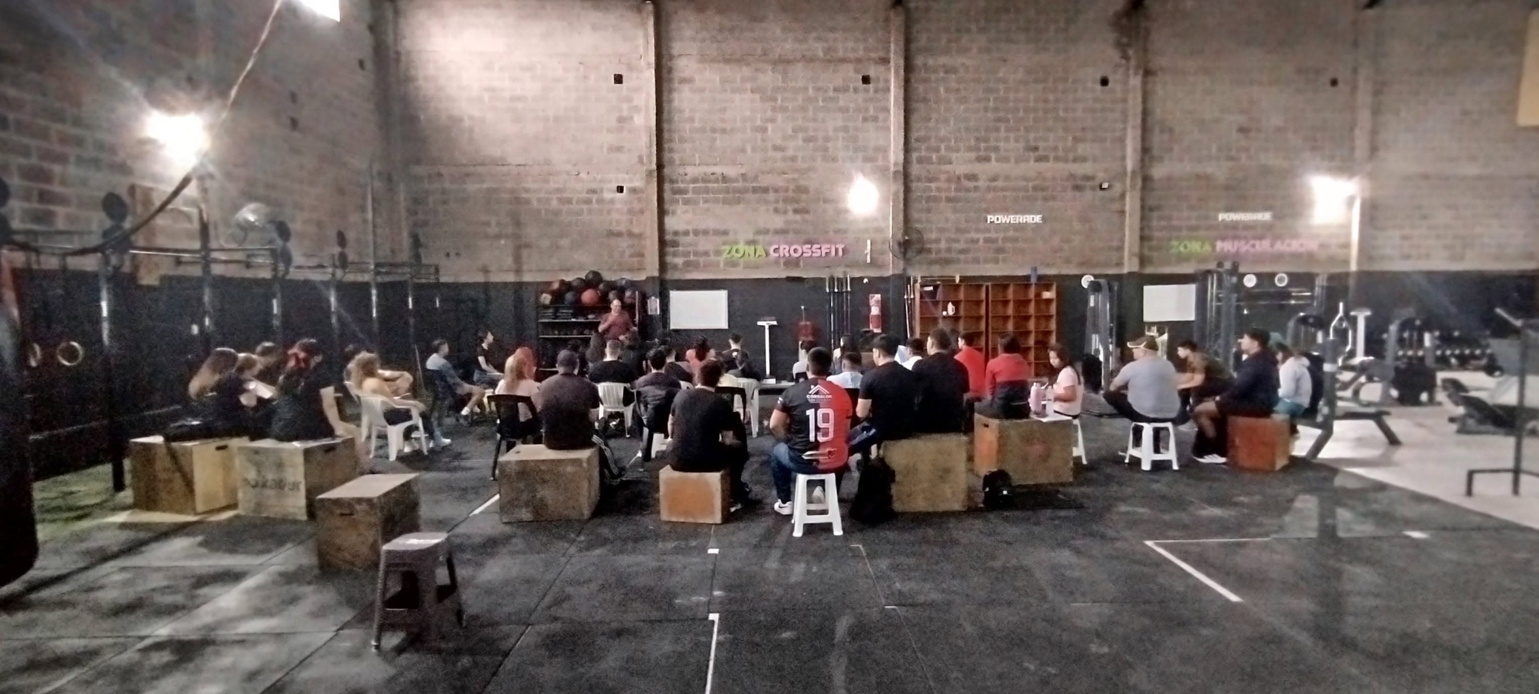 Personas sentadas en cajones de madera en un gimnasio de CrossFit durante una charla.