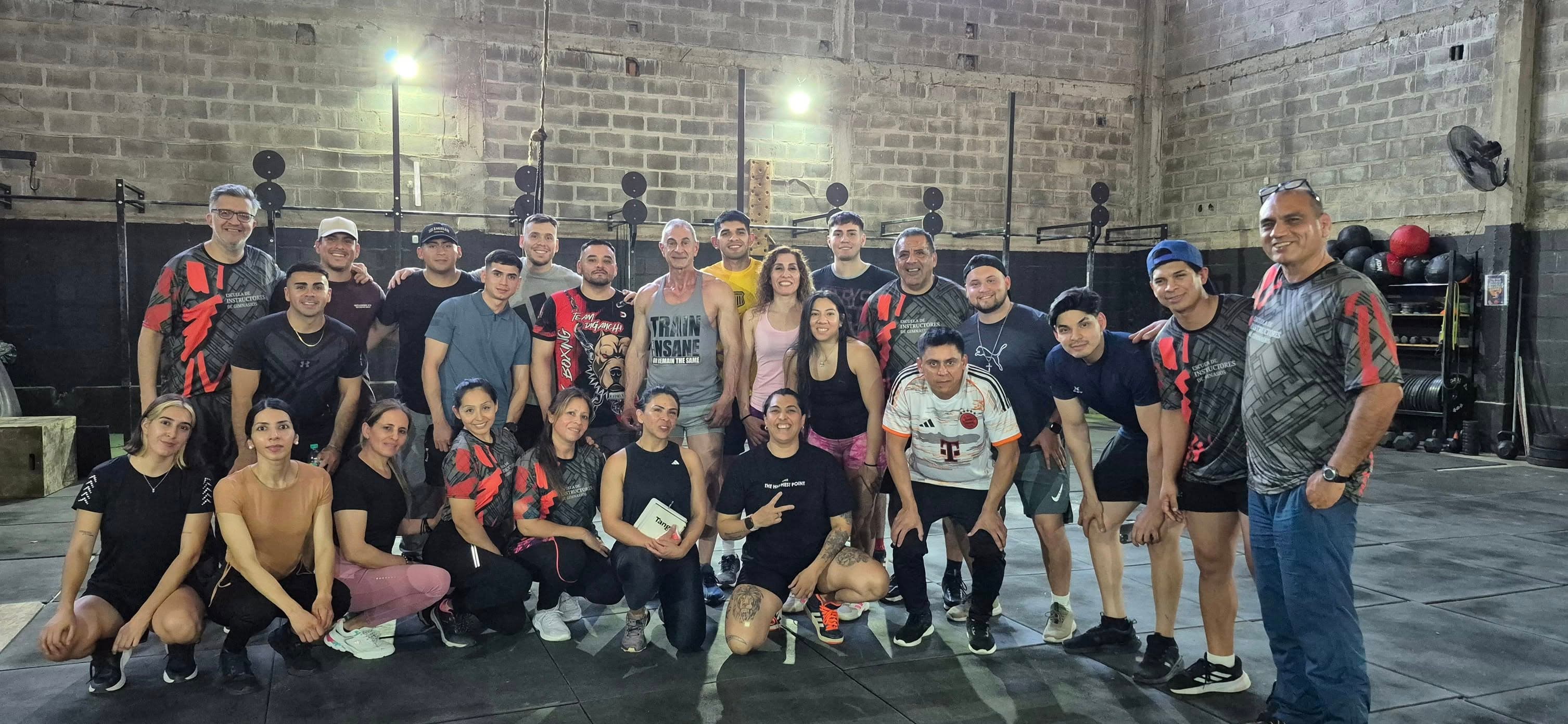 Grupo de deportistas posando sonrientes frente a una pared de ladrillos en un gimnasio.