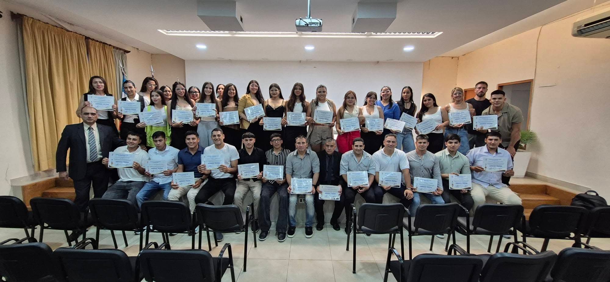 Grupo de personas posando con certificados en una ceremonia de graduación en un salón interior.