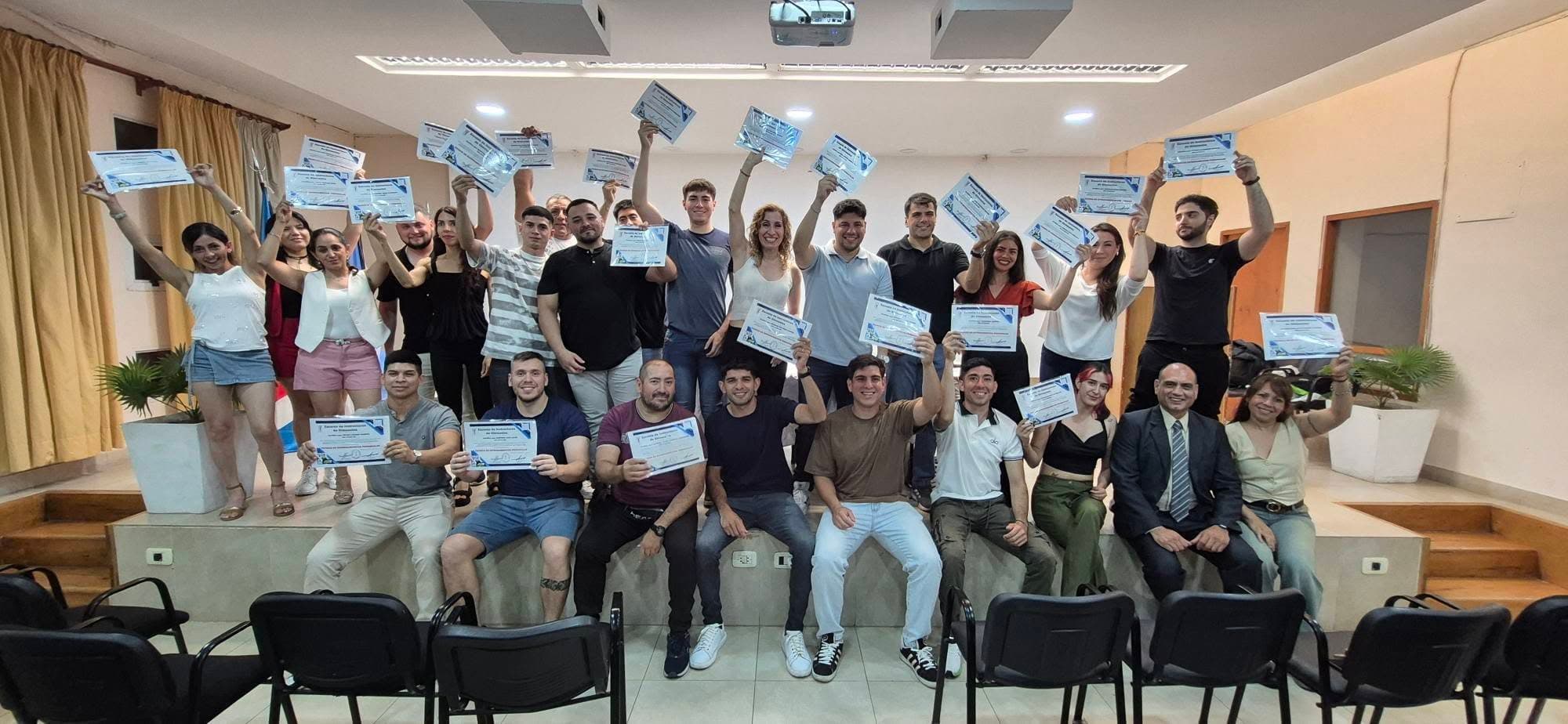Personas en un escenario sosteniendo sus certificados de graduación y sonriendo a la cámara.