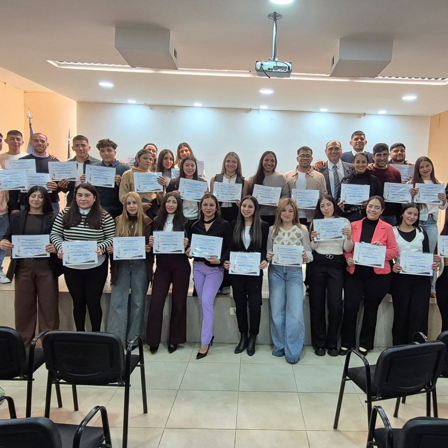 Grupo de jóvenes sonrientes posando con sus diplomas en un escenario tras una ceremonia.